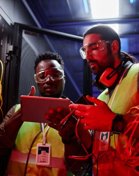 Two technicians using digital tablet setting up data network in neon light Waist up portrait of two technicians using digital tablet while repairing servers and setting up data network in neon light